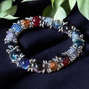 May include: A colorful beaded bracelet with silver flower-shaped charms. The beads are made of glass and have a variety of colors, including blue, green, red, orange, and purple.