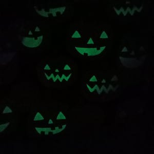 K&ouml;nnte beinhalten: Ein dunkles Bild mit mehreren leuchtend gr&uuml;nen K&uuml;rbisgesichtern. Die geschnitzten Gesichter haben dreieckige Augen, Nasen und zahnige Grinsen, die ein gruseliges Halloween-Thema erzeugen. Die K&uuml;rbisse sind &uuml;ber den dunklen Hintergrund verstreut.