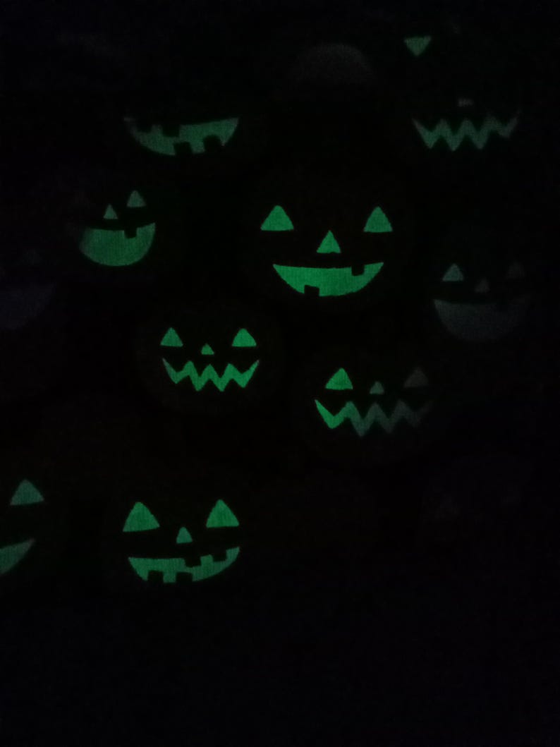 K&ouml;nnte beinhalten: Ein dunkles Bild mit mehreren leuchtend gr&uuml;nen K&uuml;rbisgesichtern. Die geschnitzten Gesichter haben dreieckige Augen, Nasen und zahnige Grinsen, die ein gruseliges Halloween-Thema erzeugen. Die K&uuml;rbisse sind &uuml;ber den dunklen Hintergrund verstreut.