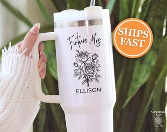 May include: White insulated tumbler with a handle, featuring the text "Future Mrs." and the name "Ellison" below a floral design. The tumbler has a white lid and a straw. An orange circle with the words "SHIPS FAST" is visible.