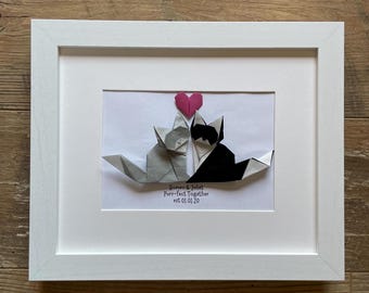 May include: A white frame with a white mat and a white background. Two origami cats, one gray and one black, are facing each other. A pink origami heart is above them. The text below the cats reads "Romeo & Juliet Purr-fect Together est 01.01.20".