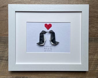 May include: A framed artwork featuring origami penguins kissing beneath a red heart. The penguins are black and white, and the frame is white. The artwork includes the text "Rachel & Ross, Mates for Life, Est. 01/01/24."