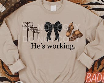 May include: A beige sweatshirt with a black bow, a pair of brown boots, and a drawing of power lines. The text "He's working." is printed on the sweatshirt.