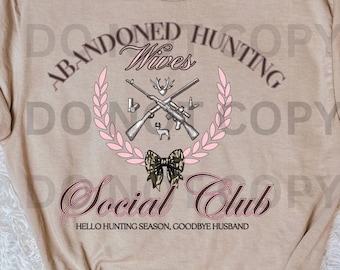 Op de afbeelding: Beige t-shirt met de tekst "Abandoned Hunting Wives Social Club". Het ontwerp bevat gekruiste geweren, een roze bloemenkrans en een camouflage strik. De tekst "Hello Hunting Season, Goodbye Husband" is ook inbegrepen.
