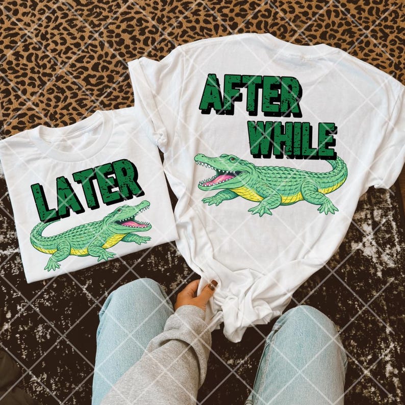 May include: White t-shirts with green text and alligator graphics. One shirt reads "LATER" and the other reads "AFTER WHILE". The alligators are green with yellow bellies and pink mouths. The shirts are on a patterned surface.