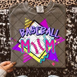 May include: A gray t-shirt with a graphic design featuring a baseball, the words "Baseball Mom" in pink and purple, and a geometric pattern in bright colors.