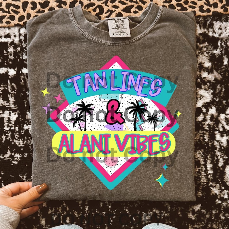 Puede incluir: Una camiseta gris con un dise&ntilde;o gr&aacute;fico que presenta una forma geom&eacute;trica rosa, azul y amarilla con el texto "Tan Lines & Alani Vibes" en una fuente retro.