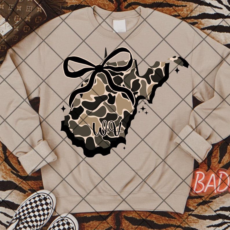 May include: A beige sweatshirt with a camouflage design in the shape of West Virginia, a black bow, and the word "WOW". The design includes black and white stars.