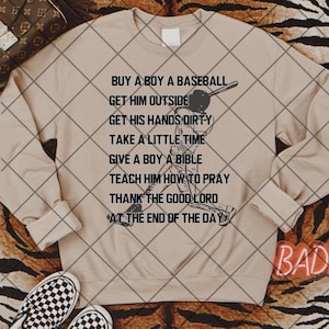 May include: Tan sweatshirt with a black baseball player graphic and the text "BUY A BOY A BASEBALL GET HIM OUTSIDE GET HIS HANDS DIRTY TAKE A LITTLE TIME GIVE A BOY A BIBLE TEACH HIM HOW TO PRAY THANK THE GOOD LORD AT THE END OF THE DAY".
