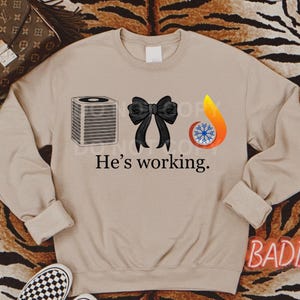 May include: A tan sweatshirt with a black bow, an air conditioner, and a flame with a snowflake inside. The text "He's working." is printed below the images.