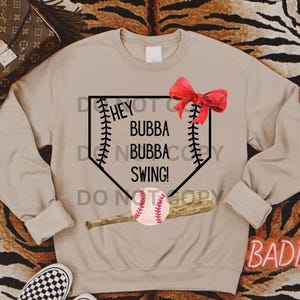Könnte beinhalten: Beigefarbener Pullover mit einem Baseball-Motiv. Das Motiv zeigt eine Homeplate, einen Baseballschläger, einen Baseball und den Text "Hey Bubba Bubba Swing!"