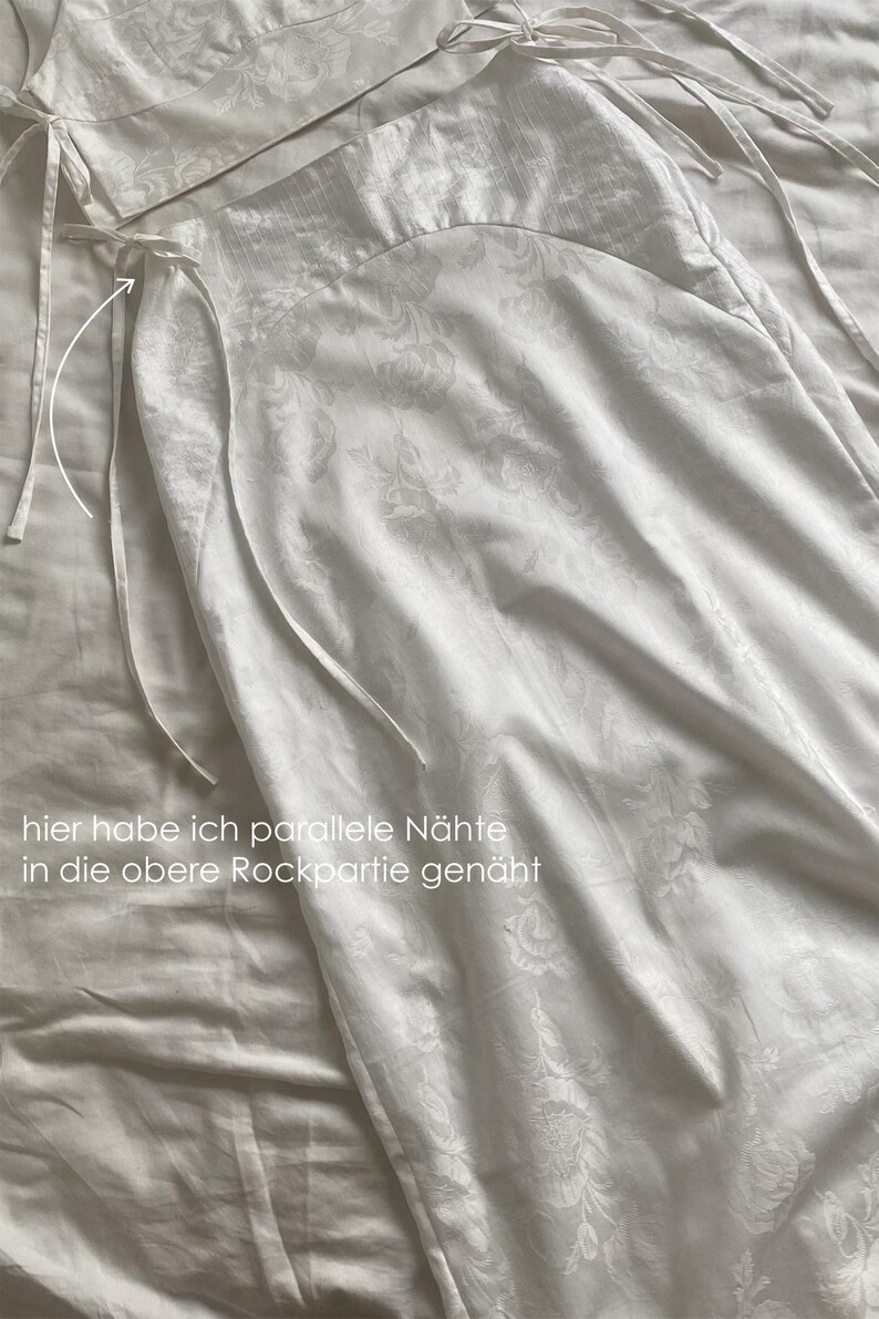 May include: White two-piece outfit with a floral pattern. The top has a halter neck and ties at the back. The skirt has a high waist and ties at the sides. The text "hier habe ich parallele N&auml;hte in die obere Rockpartie gen&auml;ht" is written on the image.