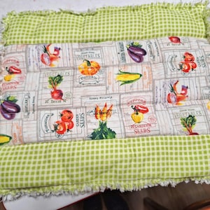 May include: A rectangular quilted pillow with a green and white gingham border. The center features a fabric panel with illustrations of various vegetables like tomatoes, pumpkins, and corn, along with the text "Vegetables" and "Garden Seeds".