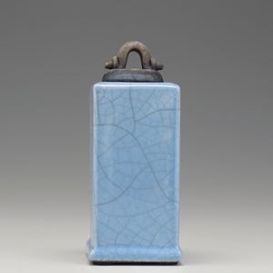 May include: A light blue ceramic jar with a crackled glaze and a metal handle on the lid.