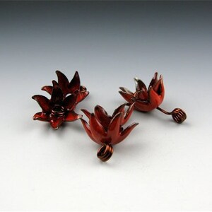 May include: Three red metal flower-shaped charms with wire loops. The charms are made of metal and have a shiny finish.
