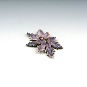 May include: A silver and purple enamel pendant in the shape of a maple leaf with a loop for hanging.