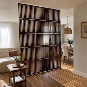 May include: A tall, dark brown wooden room divider featuring a repeating vertical slat pattern with elongated oval cutouts. The screen is composed of multiple rectangular panels connected together, creating a semi-transparent partition.