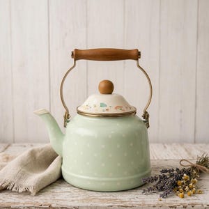 Peut inclure: Une bouilloire en émail vert menthe à pois blancs, avec une poignée en bois et un couvercle à motifs floraux. La bouilloire a un cadre et un bec en métal doré. Un tissu en lin et des fleurs séchées sont à côté de la bouilloire sur une surface en bois vieilli.