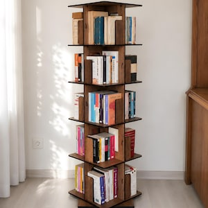 May include: A tall, rotating wooden bookshelf with five tiers of shelving. The unit features a dark brown finish and is organized into four quadrants per level, filled with various books of different sizes, colors, and thicknesses.