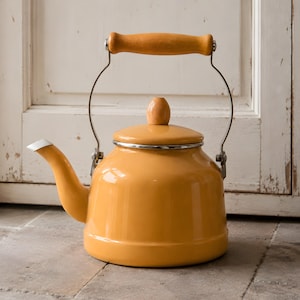 May include: A yellow enamel tea kettle with a wooden handle and lid knob. The kettle has a silver rim and spout with a white tip. The handle is made of light-colored wood and is arched. The kettle is sitting on a stone surface.