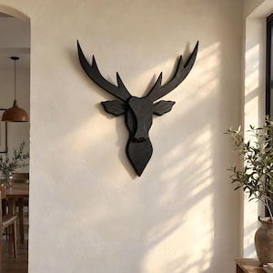 Könnte beinhalten: Eine an der Wand montierte Hirschkopf-Skulptur aus dunkel schwarzem Holz. Das Stück zeichnet sich durch ein geometrisches, stilisiertes Design mit markanten, geschwungenen Geweihen und einer glatten, matten Oberfläche aus.