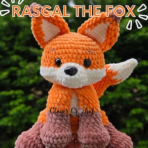 May include: A handmade crocheted fox toy, predominantly orange with white and brown accents. The fox features large ears, a white face, and black eyes. The text "RASCAL THE FOX" is above the fox, and "Clever Crochet" is below.