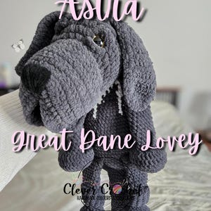 May include: A handmade gray crochet Great Dane lovey. The lovey has a large head, floppy ears, and a long body with rounded feet. The text "In Loving Memory Astra" and "Great Dane Lovey" are displayed in pink script.