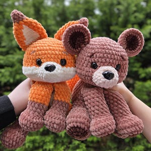May include: Two handmade crochet stuffed animals: an orange fox with white accents and a brown bear. The fox has a white face and brown feet. The bear is a soft brown color with a black nose and small ears.