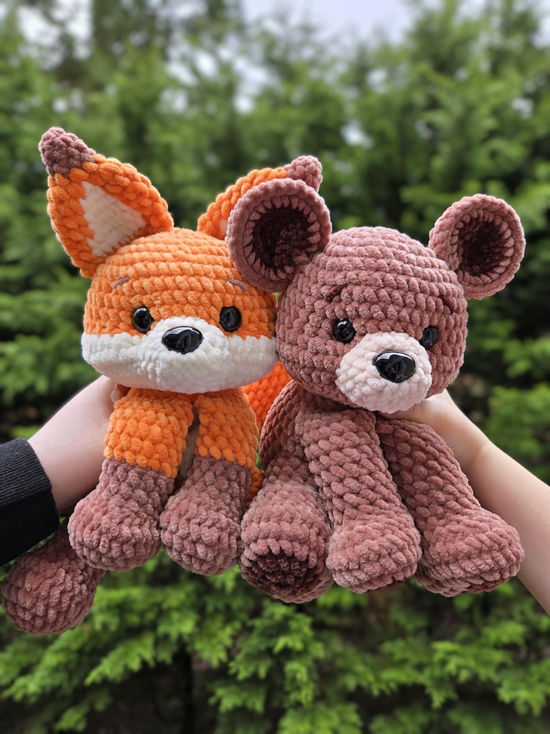 May include: Two handmade crochet stuffed animals: an orange fox with white accents and a brown bear. The fox has a white face and brown feet. The bear is a soft brown color with a black nose and small ears.