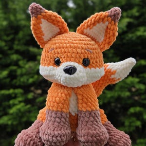May include: A handmade orange and white crochet fox plush toy with a black nose and black eyes. The fox has brown accents on its ears and feet. The plush toy is soft and cuddly, perfect for a child's room or as a decorative item.