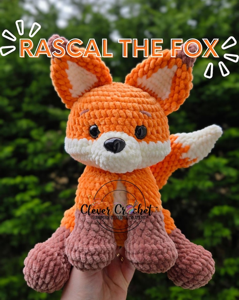 May include: A crocheted fox plush toy in shades of orange, white, and brown. The fox has large ears, a white muzzle, and black eyes. The text "RASCAL THE FOX" is above the fox, and "Clever Crochet" is below.