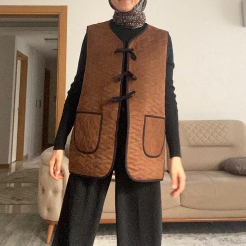 May include: A brown quilted vest with a black trim and a tie closure. The vest has two pockets on the front.
