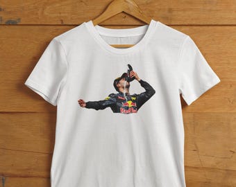 May include: White t-shirt with a printed image of a race car driver drinking from a bottle with the word "Red Bull" on it.