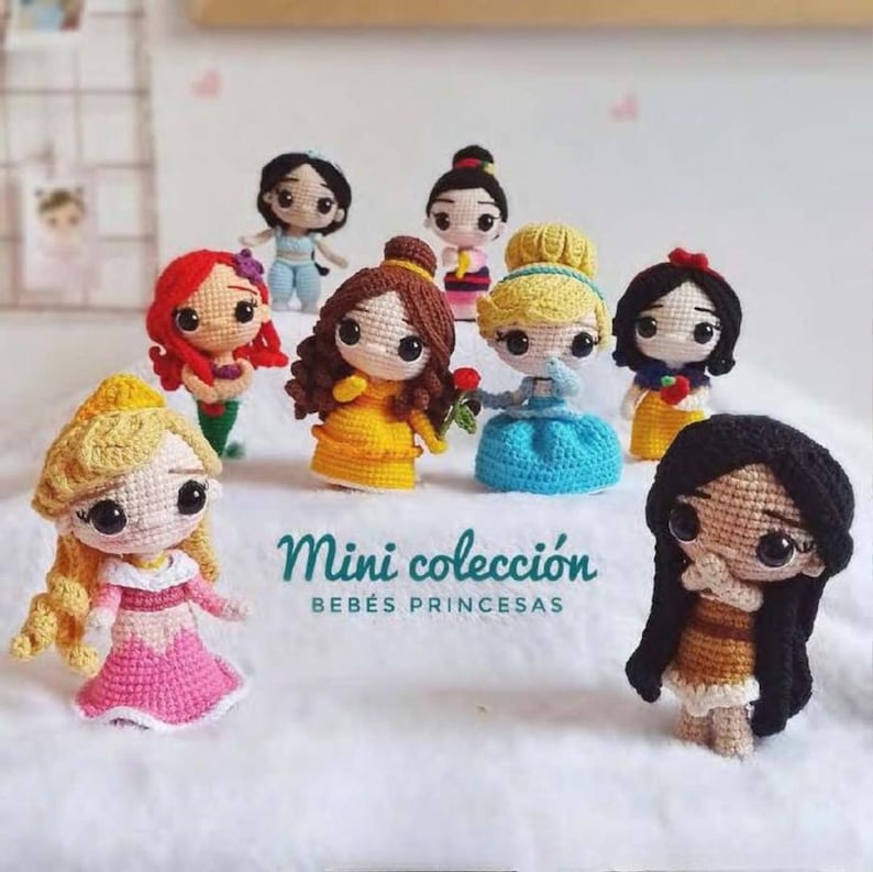 May include: A selection of crocheted princess dolls, each with distinct hairstyles and clothing. The dolls are in various colours, including yellow, blue, red, and pink. The text "Mini colecci&oacute;n BEB&Eacute;S PRINCESAS" is visible.