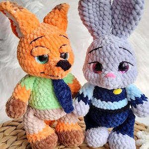 May include: Two handmade crochet toys: an orange fox with green and blue details and a grey bunny with blue and white accents. Both have detailed faces and are made with soft, textured yarn. The toys are displayed on a woven surface.