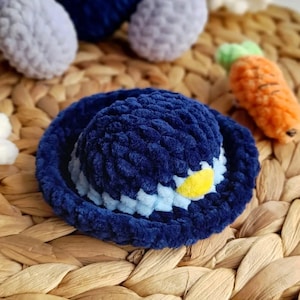 May include: A navy blue crocheted hat with a light blue and yellow accent. The hat is made of a soft, plush material and has a rounded crown and a wide brim. The hat is part of a set of crocheted toys.