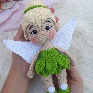 Puede incluir: Una muñeca de hada de crochet con cabello rubio, un vestido verde, alas blancas y zapatos verdes.