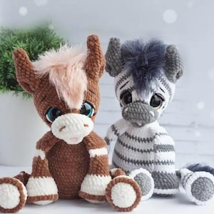 May include: Two handmade crochet soft toys: a brown horse with a pink mane and a grey and white zebra. Both have large, expressive eyes and are sitting down. The horse has white accents on its legs and the zebra has grey stripes.