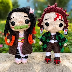 May include: Two handmade crochet dolls featuring large black eyes. The left doll has long black hair with orange tips, a pink kimono, and a green bamboo muzzle. The right doll has dark red hair, a green and black checkered haori, and hanafuda earrings.