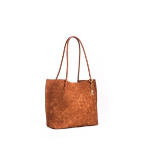 May include: A brown woven leather tote bag with long handles. The bag has a rectangular shape and a woven pattern. A small gold-colored charm hangs from one of the handles. The bag is set against a white background.