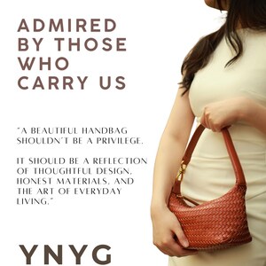 May include: A woven, reddish-brown handbag with a curved shape and a short handle is held by a person wearing a cream-colored dress. The bag has a gold-colored clasp. Text on the left reads "ADMIRED BY THOSE WHO CARRY US" and "YNYG".