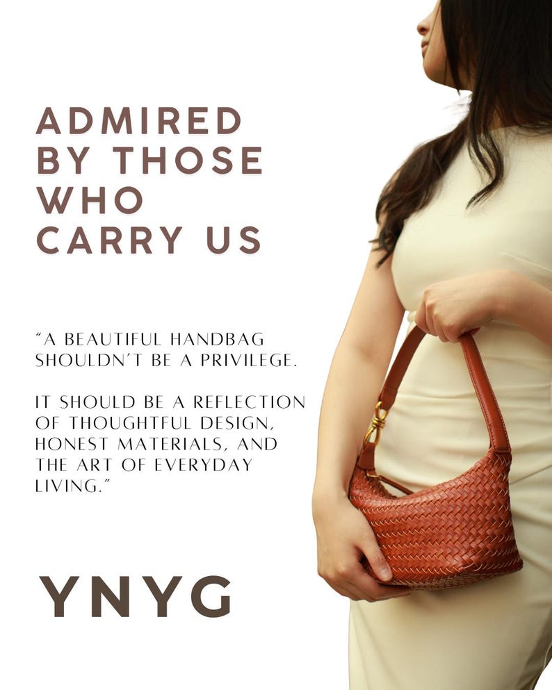 May include: A woven, reddish-brown handbag with a curved shape and a short handle is held by a person wearing a cream-colored dress. The bag has a gold-colored clasp. Text on the left reads "ADMIRED BY THOSE WHO CARRY US" and "YNYG".