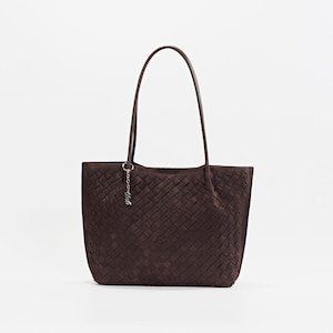 May include: A dark brown tote bag with a woven pattern. The bag has two long handles and a small silver charm attached to one side. The bag is made of a soft material and is suitable for everyday use.