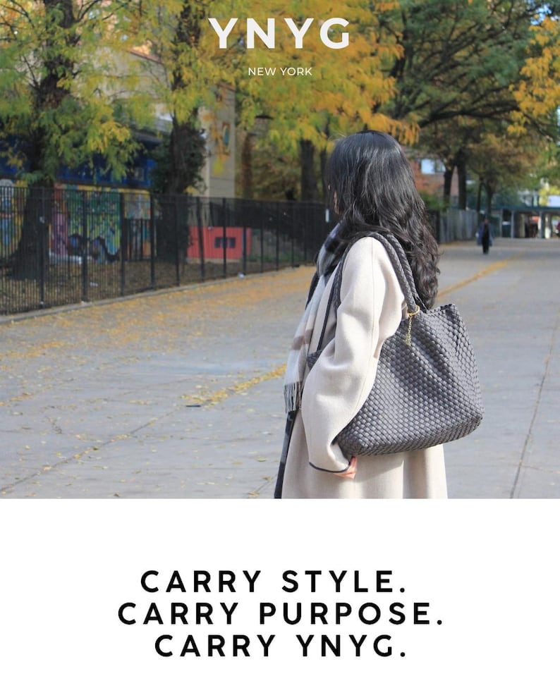 May include: A woman stands outdoors, wearing a light-colored coat and carrying a gray woven tote bag. The bag has a structured shape and a shoulder strap. The text "YNYG NEW YORK" is at the top, and "CARRY STYLE. CARRY PURPOSE. CARRY YNYG." is at the bottom.
