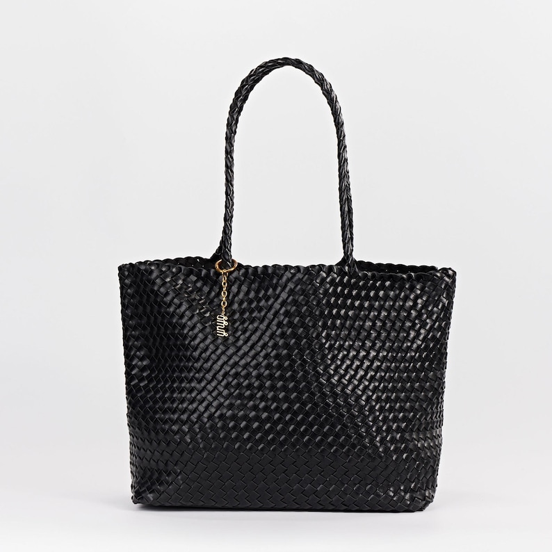 Pode incluir: Bolsa tote preta tecida com al&ccedil;as tran&ccedil;adas. A bolsa tem formato retangular e um padr&atilde;o tecido. Um berloque dourado com a palavra "shut" pende da al&ccedil;a. A bolsa est&aacute; em um fundo branco.