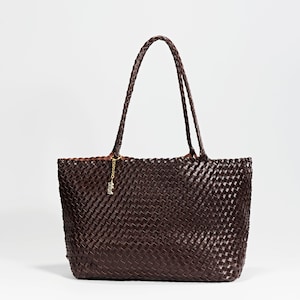 Pode incluir: Uma bolsa tote tecida marrom escuro com al&ccedil;as tran&ccedil;adas. A bolsa tem formato retangular e um pingente dourado pendurado na al&ccedil;a. A bolsa &eacute; feita de um material tecido, e as al&ccedil;as tamb&eacute;m s&atilde;o tran&ccedil;adas.