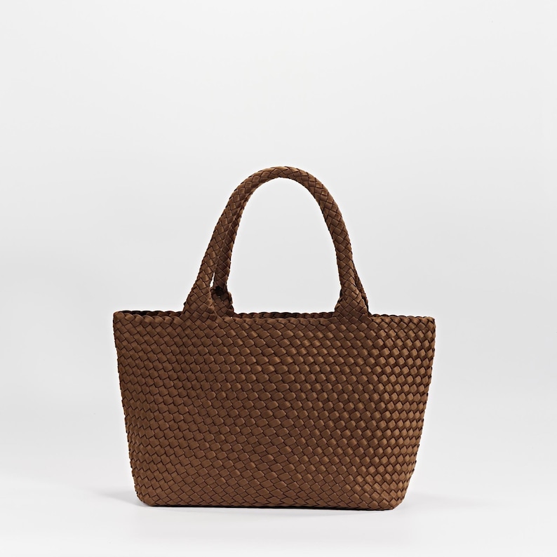 May include: A brown tote bag with woven texture. The bag has two braided handles and a rectangular shape. The bag is made of a durable material and is suitable for carrying various items.
