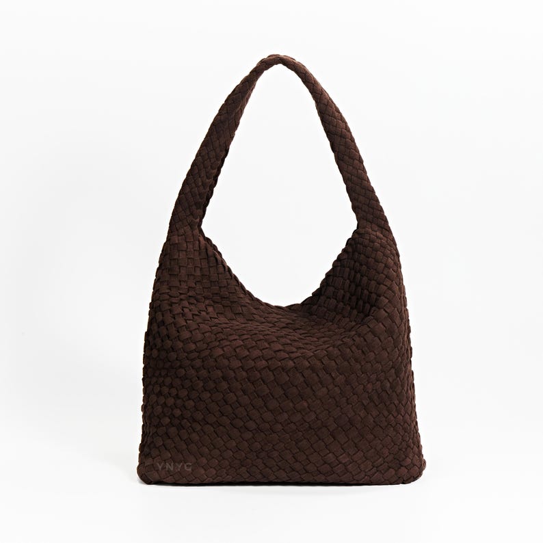 K&ouml;nnte beinhalten: Eine braune Schultertasche mit einem einzelnen Riemen. Die Tasche hat einen rechteckigen Boden und eine abgerundete Oberseite mit einer gewebten Textur. Die Tasche ist aus einem weichen Material gefertigt und f&uuml;r den t&auml;glichen Gebrauch geeignet.