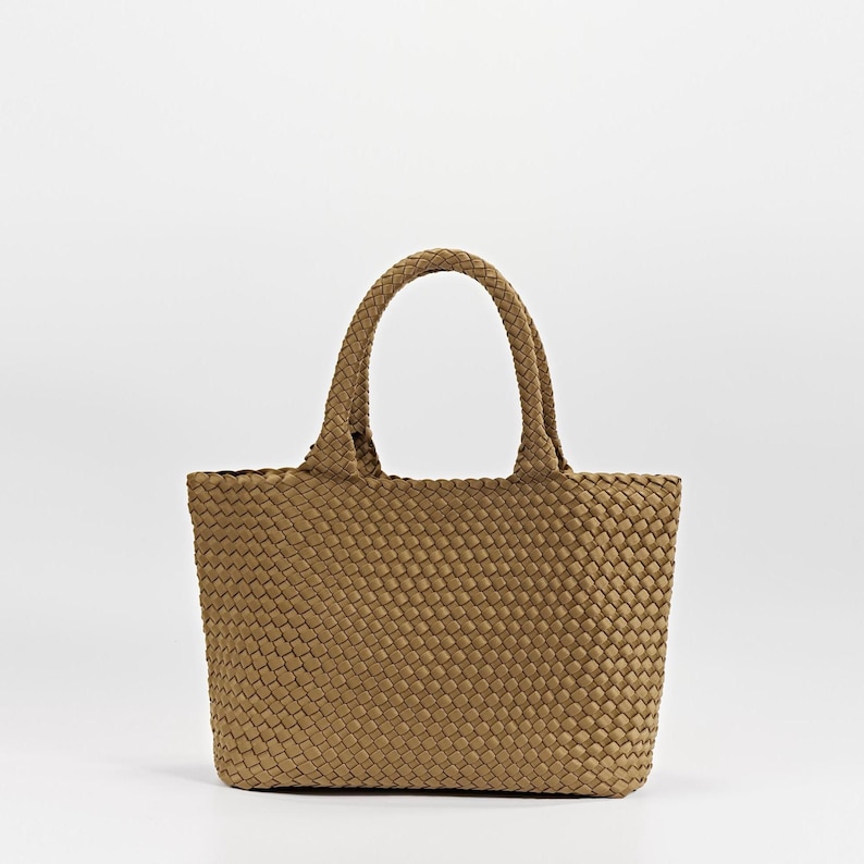 May include: A woven tote bag in a light brown color. The bag has two braided handles and a rectangular shape. The weave pattern is consistent throughout the bag's body and handles. The bag is empty and sits against a white background.