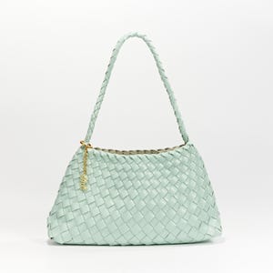 Peut inclure: Un sac à main vert clair tissé avec une poignée tressée. Le sac a une forme rectangulaire avec un fond arrondi et un charm doré suspendu à la poignée. La doublure intérieure est de couleur neutre.